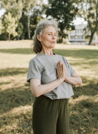 Elderly woman meditating and practicing yoga in a sunny park, embracing wellness and mindfulness.
